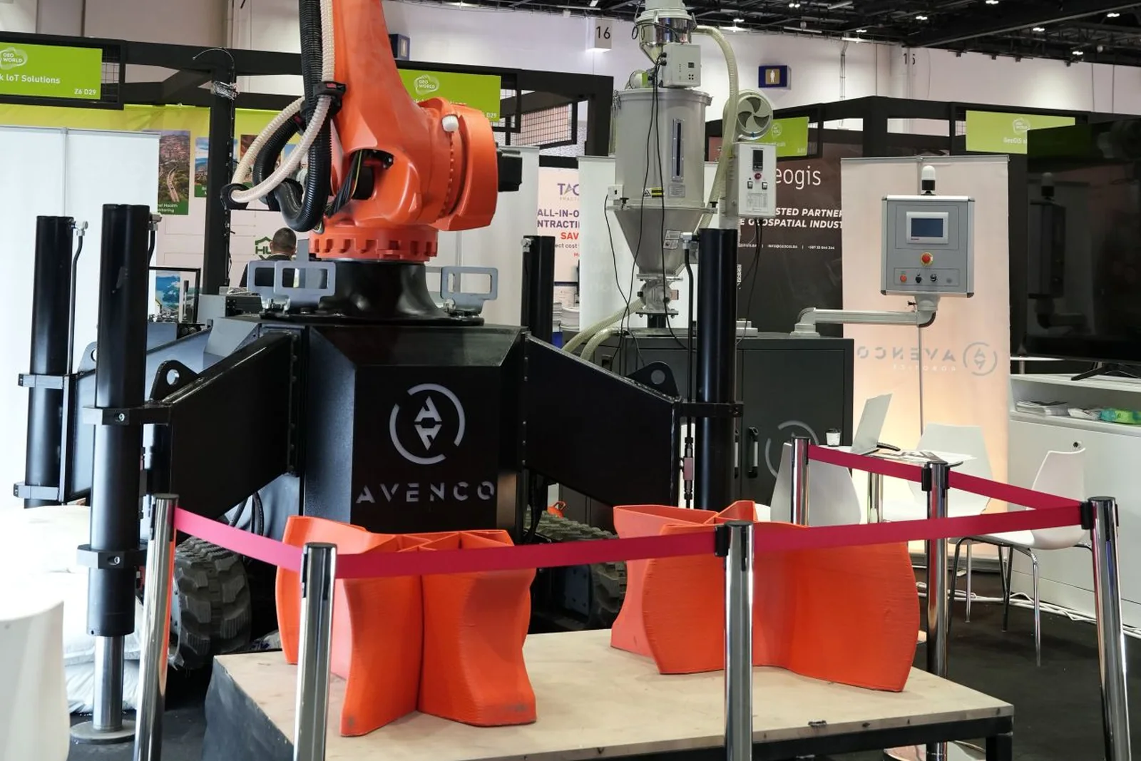 The robotic printing arm on the stand, with printed concrete pieces on the platform beneath it