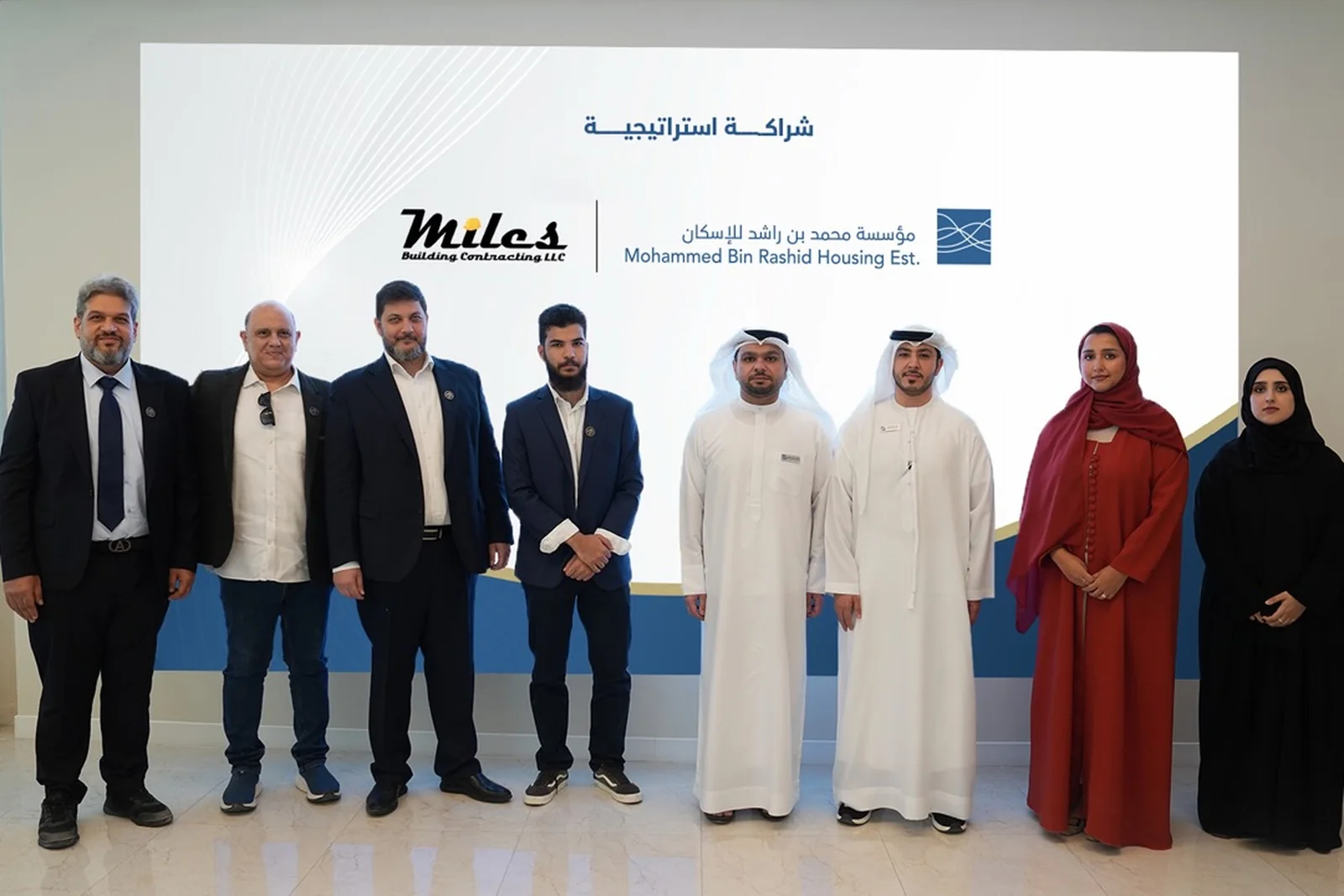 The Miles Building Contracting and Mohammed Bin Rashid Housing Establishment teams together after the signing, in front of a backdrop carrying both organisations' logos