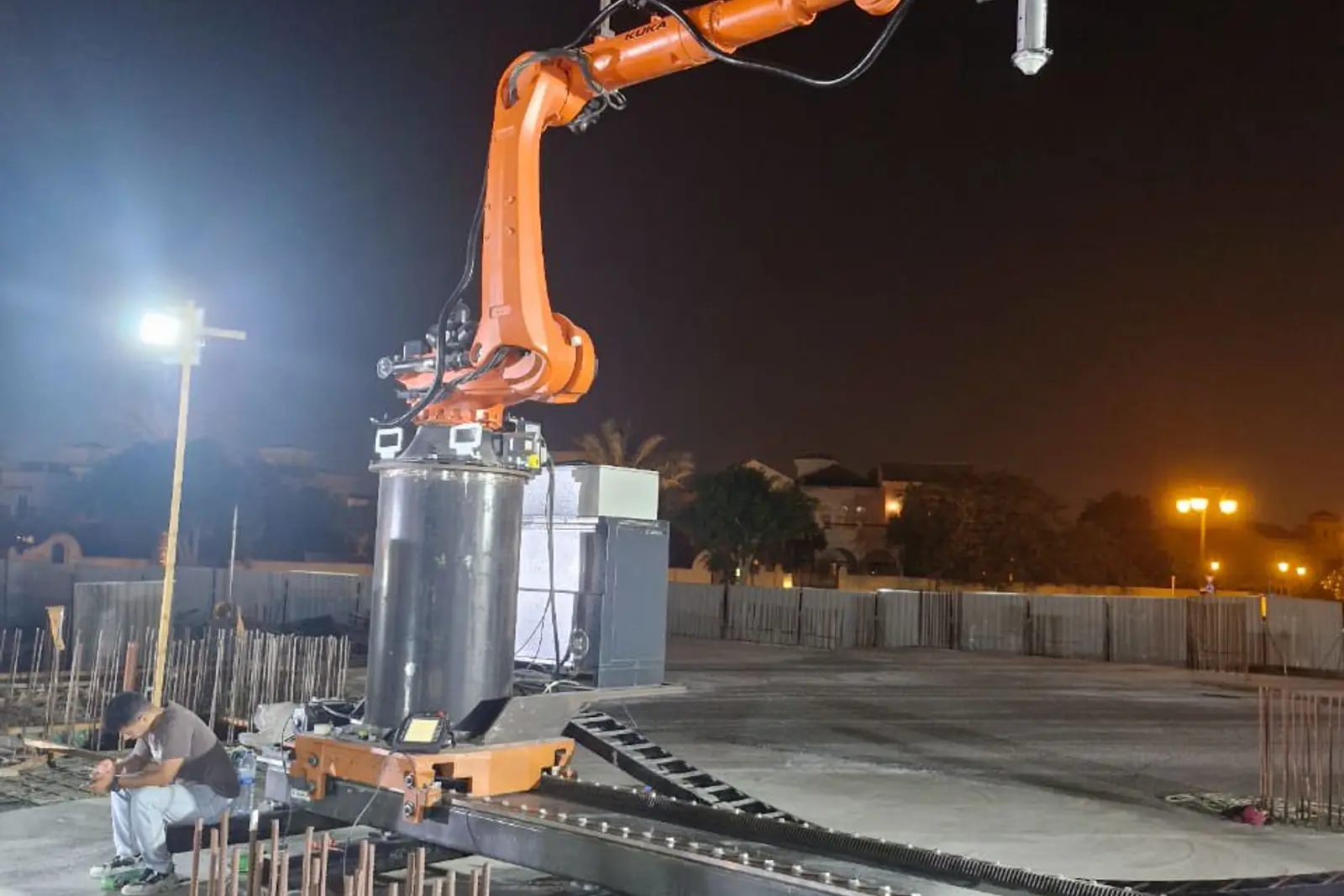 A robotic arm 3D printing concrete on a Miles site at night